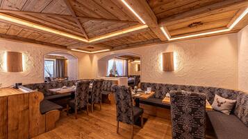A restaurant with wooden ceiling beams, arched windows, and patterned upholstered seating.