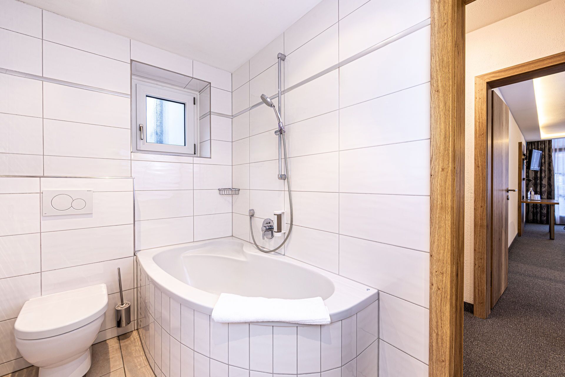 A modern bathroom with white tiles, a bathtub, a toilet, and a shower.