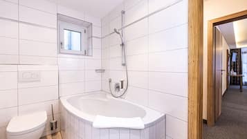A modern bathroom with white tiles, a bathtub, a toilet, and a shower.