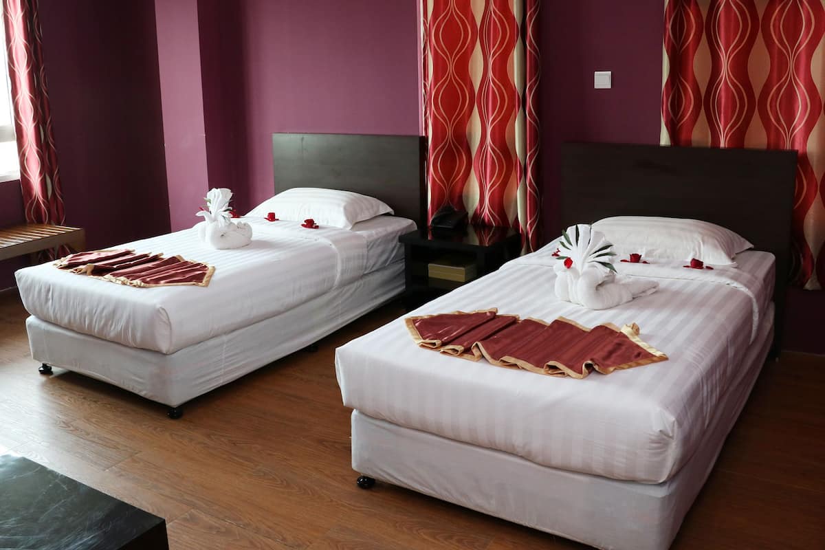 Deux lits avec du linge de lit blanc, des rideaux à motifs rouges et blancs, et un plancher en bois.