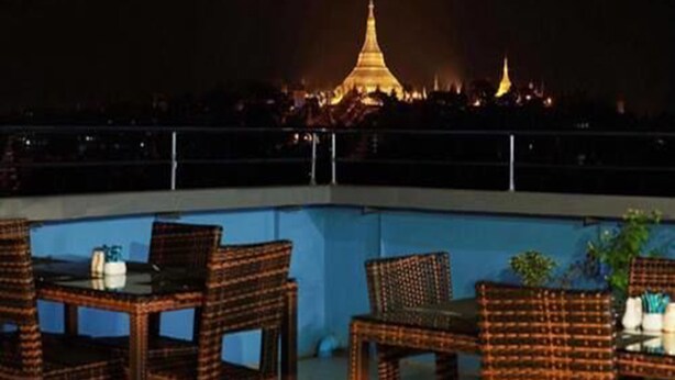 Una terraza en la azotea con mobiliario de mimbre y vistas a una pagoda iluminada en la noche.