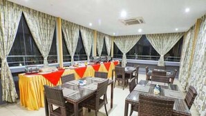 Un comedor con mesas y sillas, ventanas amplias con cortinas y suelo de baldosas.