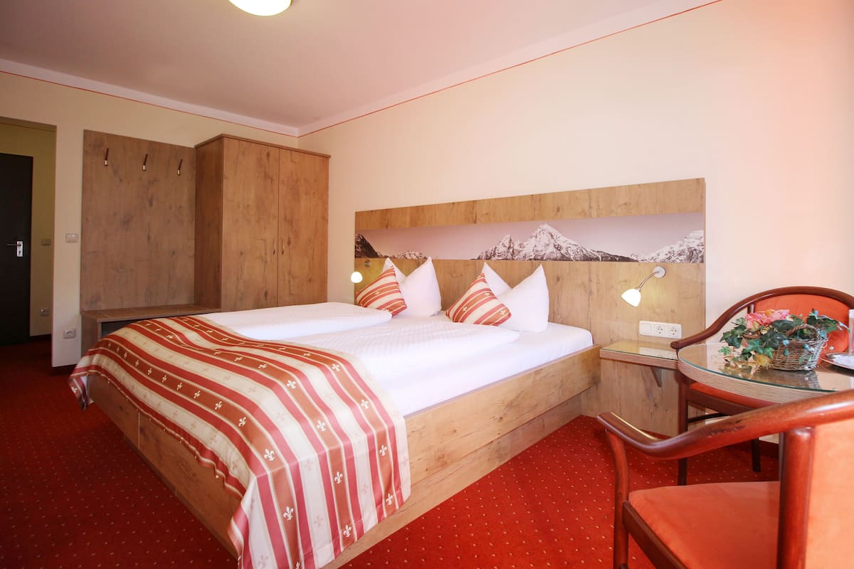 A hotel room with a large bed, wooden headboard, a desk with a chair, and a wall-mounted lamp.