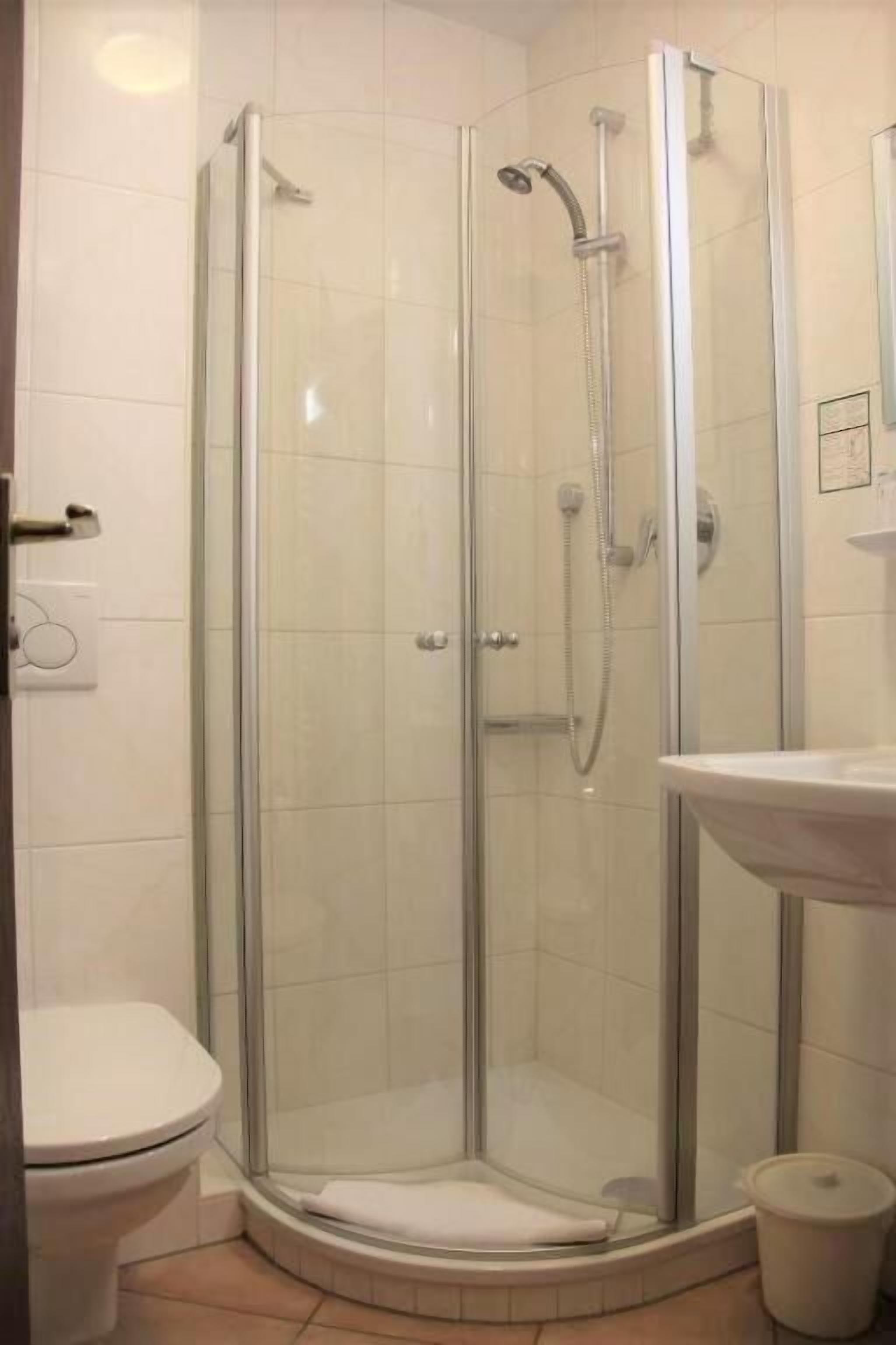 A glass-enclosed shower stall with a handheld showerhead and a wall-mounted faucet.