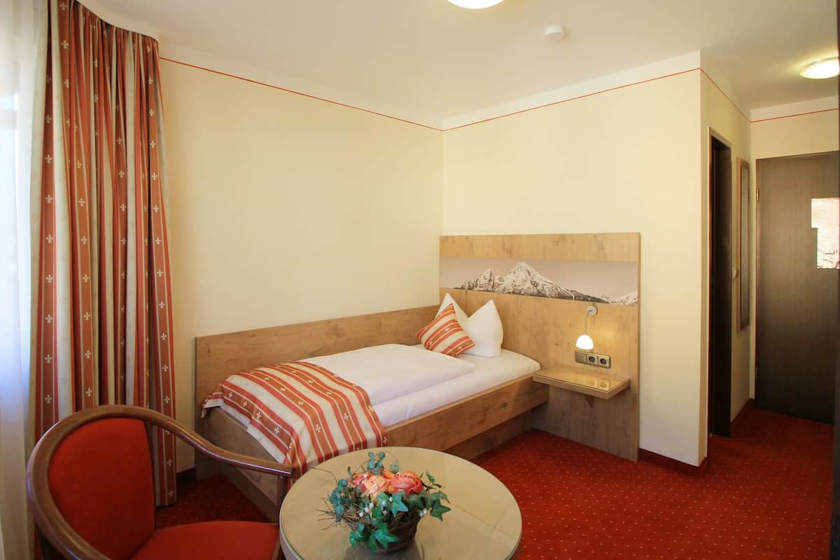 A hotel room with a bed, a nightstand, a lamp, a chair, and a small table with a flower arrangement.