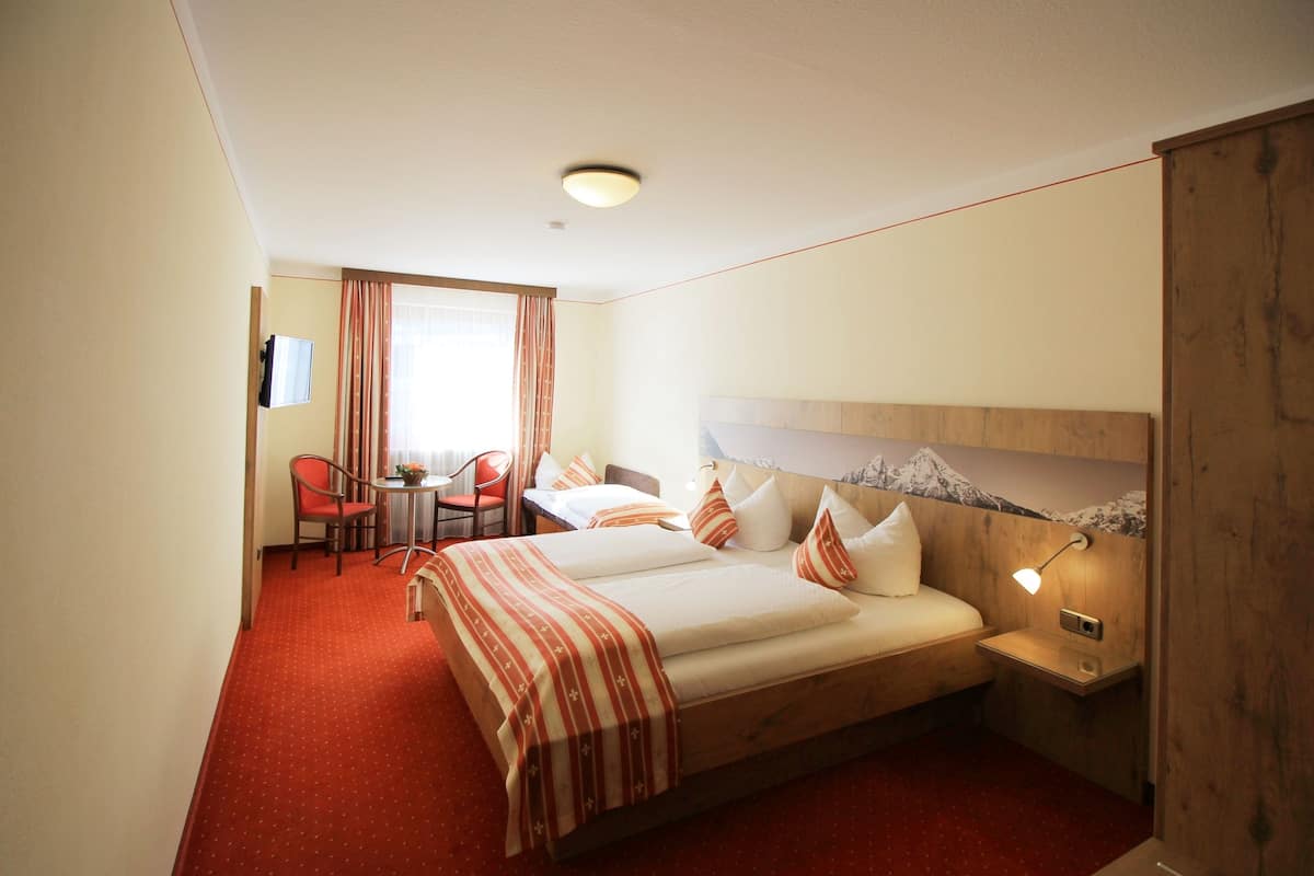 A hotel room with a bed, bedside table, lamp, and a desk with a chair.