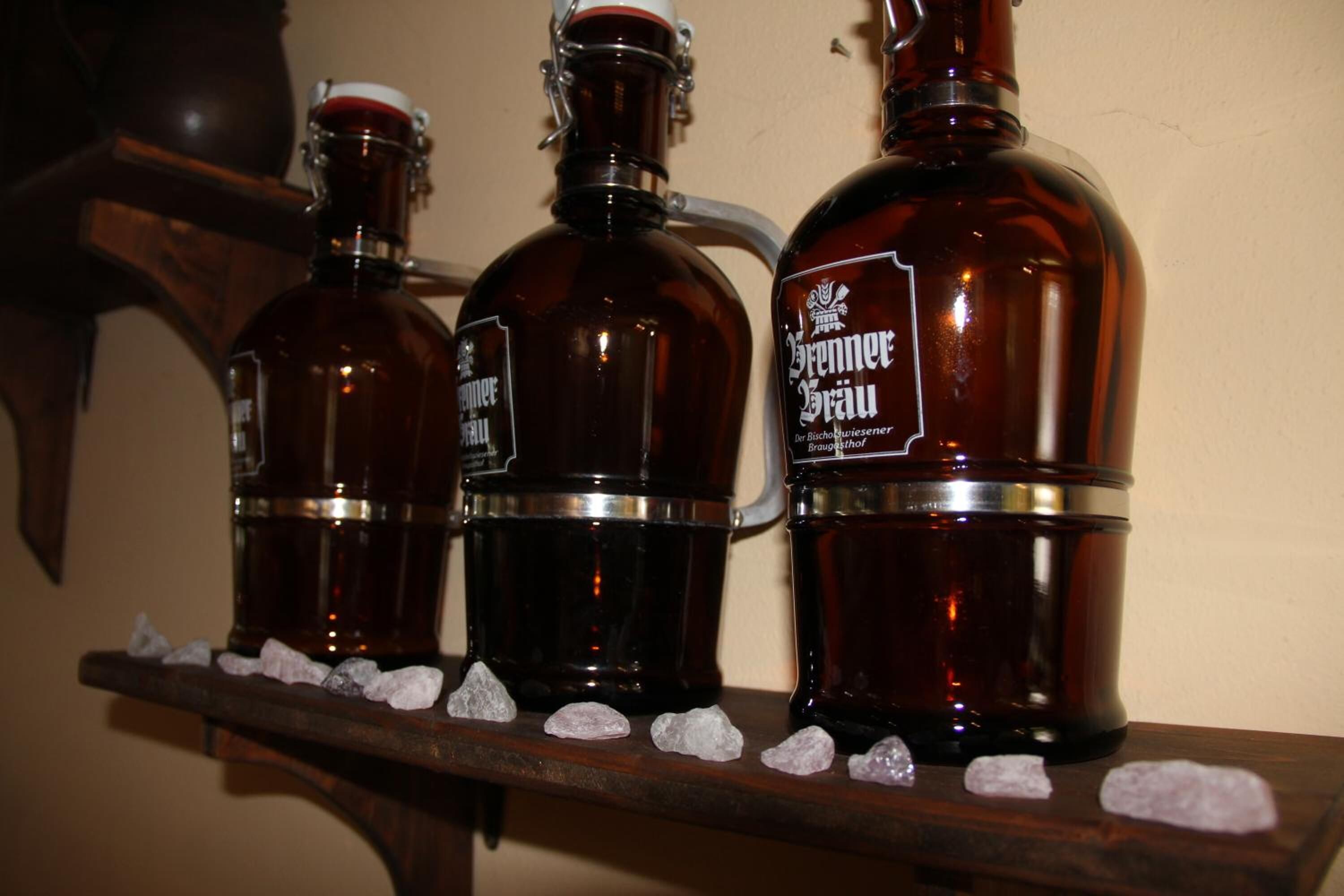 Three large brown bottles with metal bands and labels on a wooden shelf.