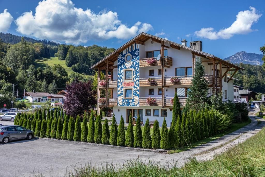 Ein mehrstöckiges Hotel mit Balkonen, umgeben von ordentlich geschnittenen Hecken und einer Bergkulisse.