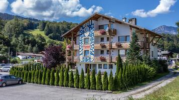Ein mehrstöckiges Hotel mit Balkonen, umgeben von ordentlich geschnittenen Hecken und einer Bergkulisse.