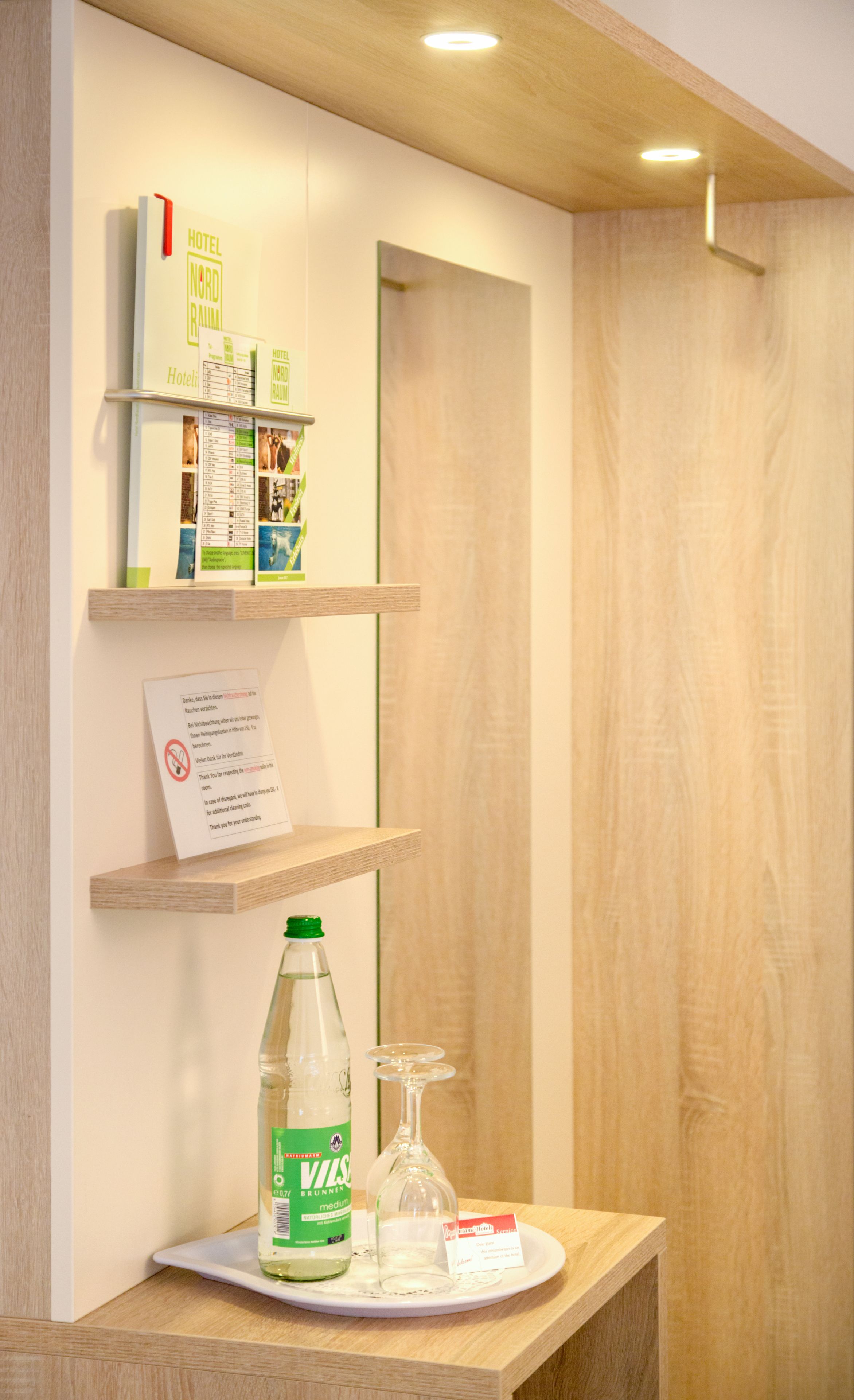 A reception area with a wooden reception desk, a bottle of Voss water, a glass, and a small tray with a card.