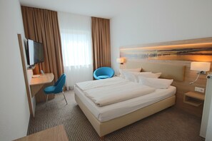 A hotel room with a large bed, a desk with a chair, a television, and a headboard with a light. - Hotel NordRaum (Bremen)