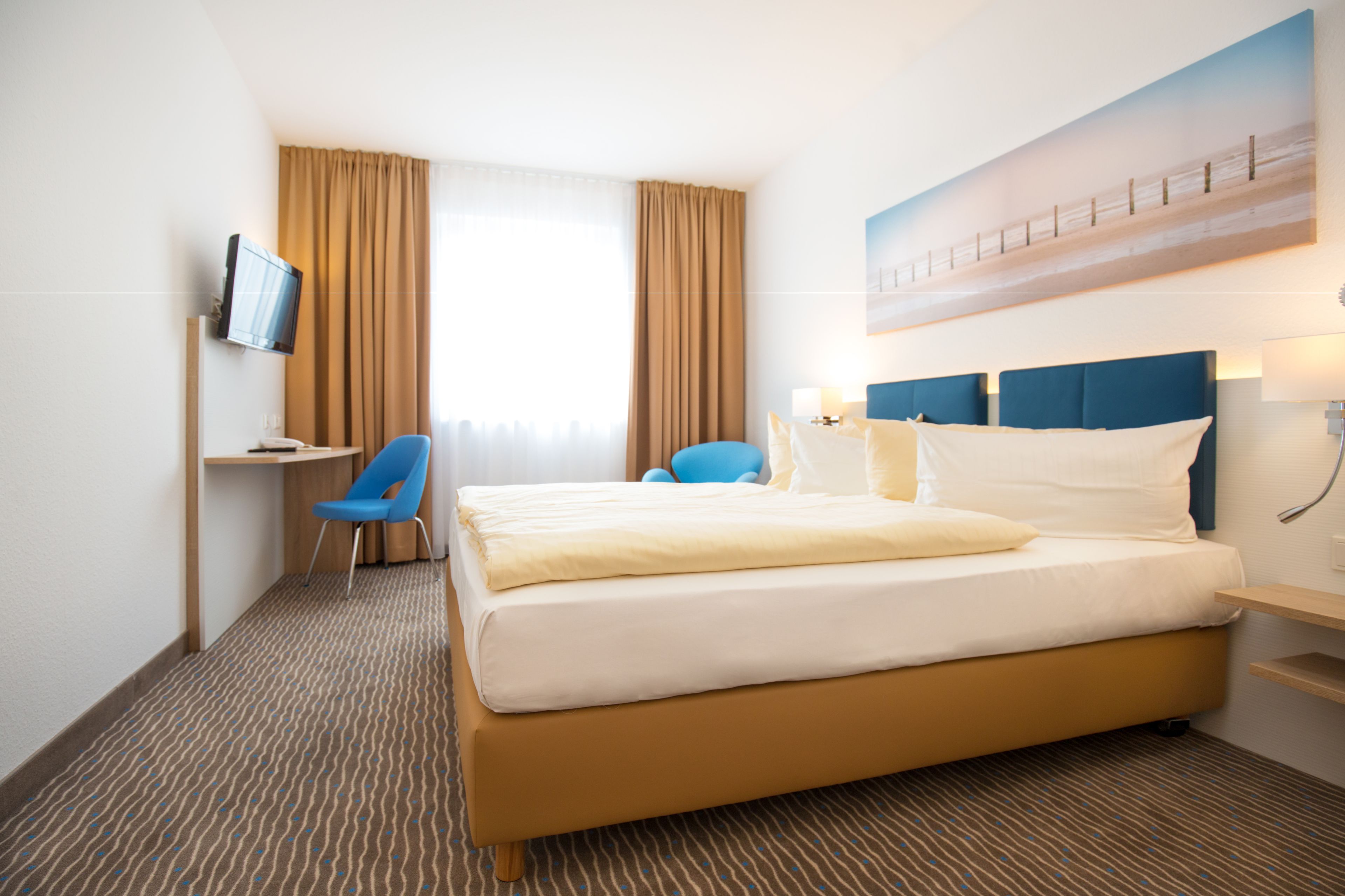 Habitación de hotel con cama, escritorio con silla, televisión y un cuadro en la pared.