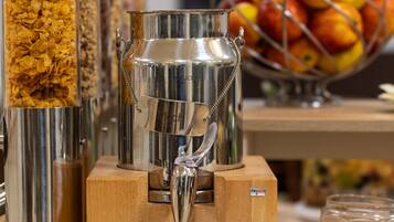 A beverage dispenser with a metal container and a wooden base, surrounded by glass containers of cereal.