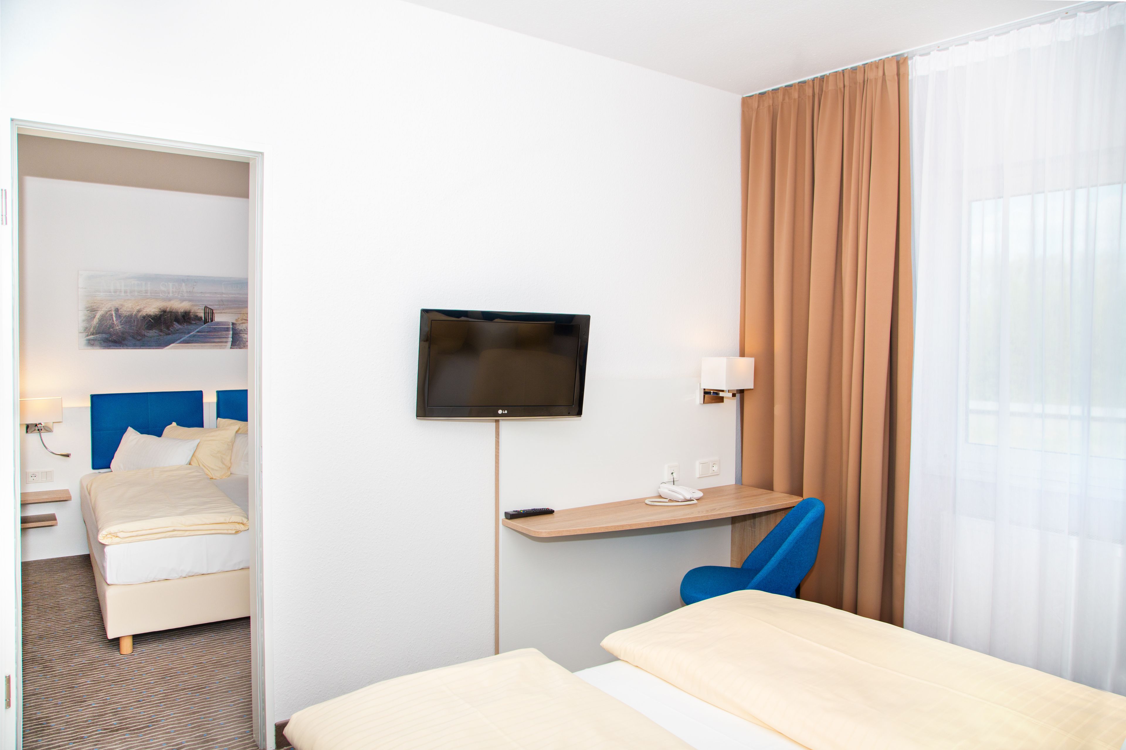 Une chambre d’hôtel comprenant un lit, un bureau avec une chaise, une télévision et une fenêtre avec des rideaux.