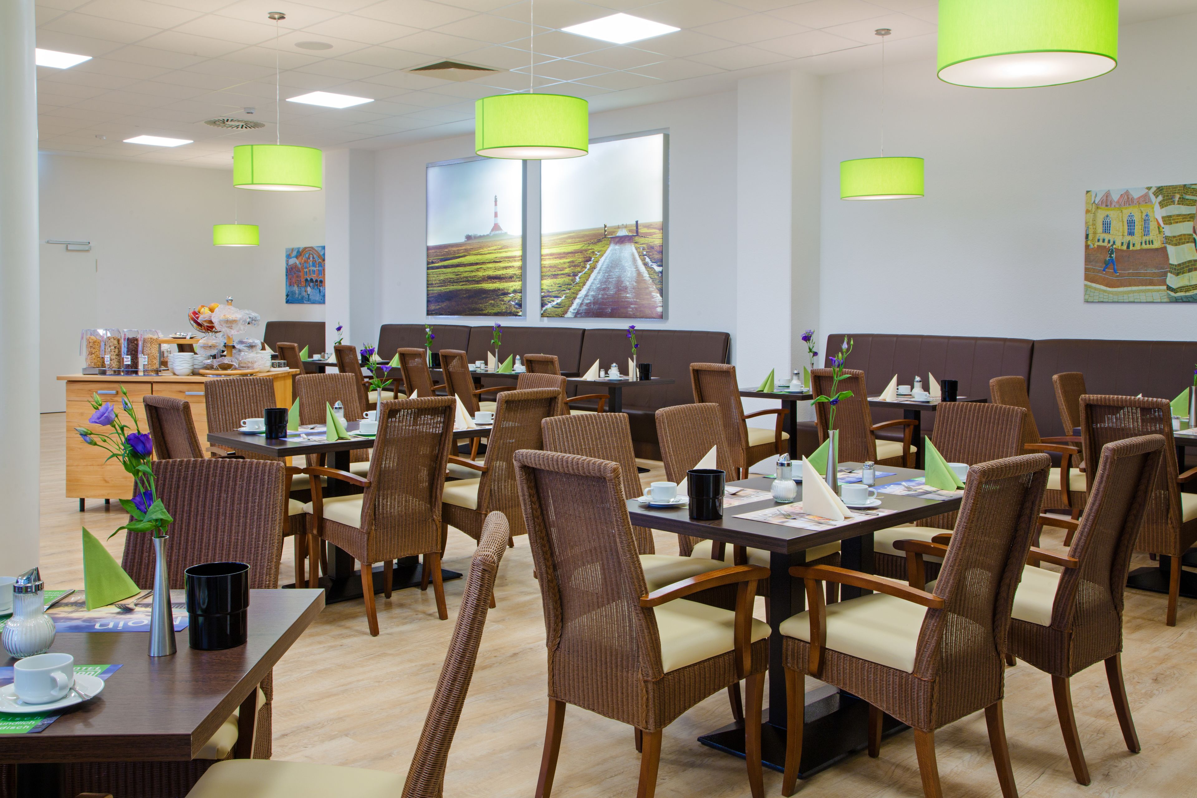 A restaurant with wicker chairs and tables, a buffet area, and large windows with a view of a road.