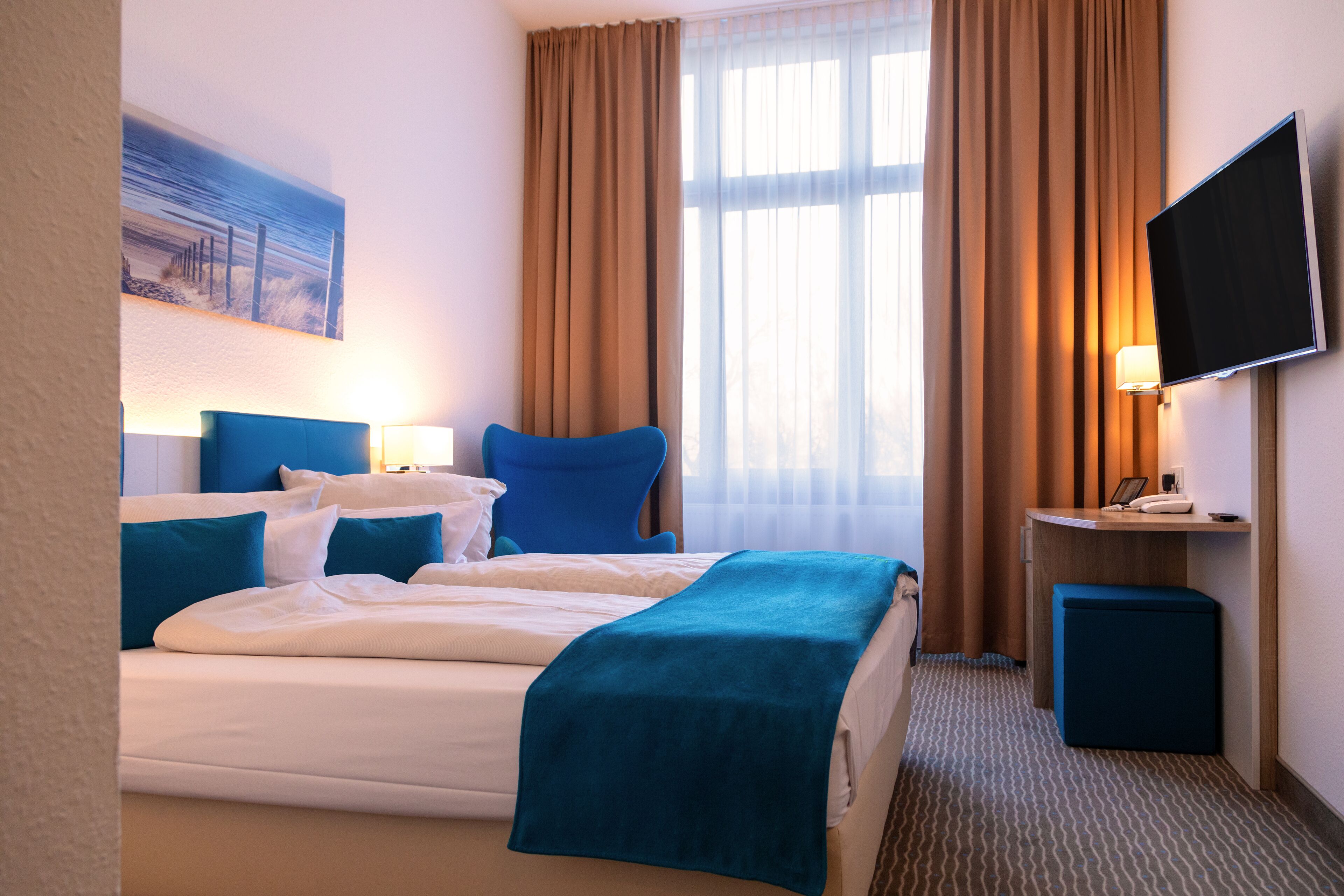 Une chambre d’hôtel avec un lit, un bureau, une télévision et une fenêtre avec des rideaux.