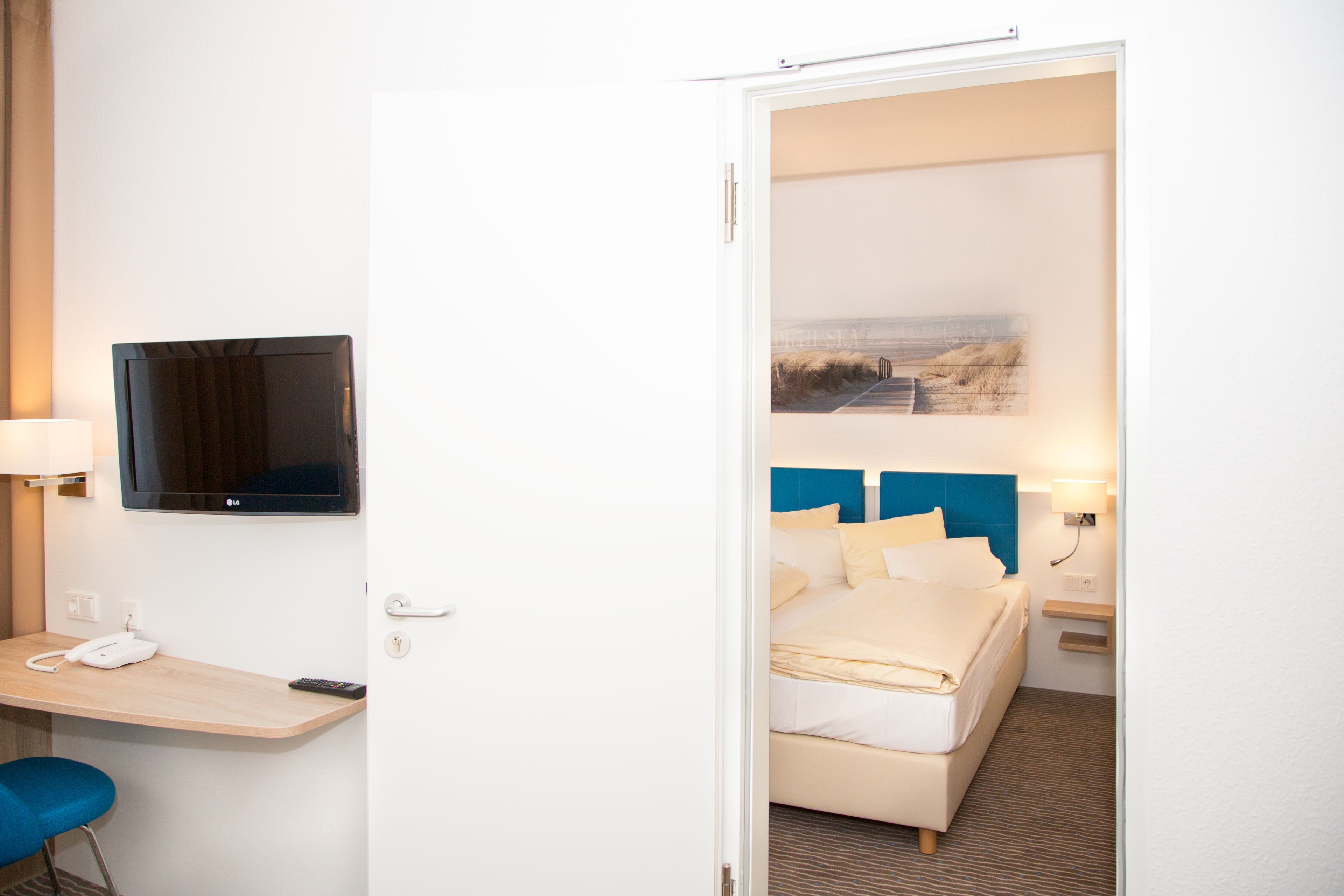Una habitación de hotel con una cama, un escritorio con teléfono, una televisión y un cuadro en la pared.
