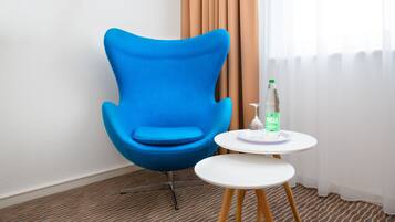 Una habitación con una silla azul, una mesita blanca con una botella y una alfombra estampada.