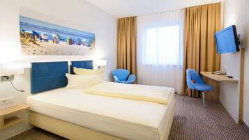 A hotel room with a large bed, a desk with a computer, a TV, and a chair.