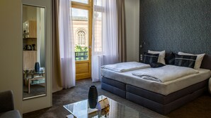 Une chambre d’hôtel moderne avec un grand lit, une table basse en verre, un miroir et une vue sur une cour intérieure, visible par la fenêtre.