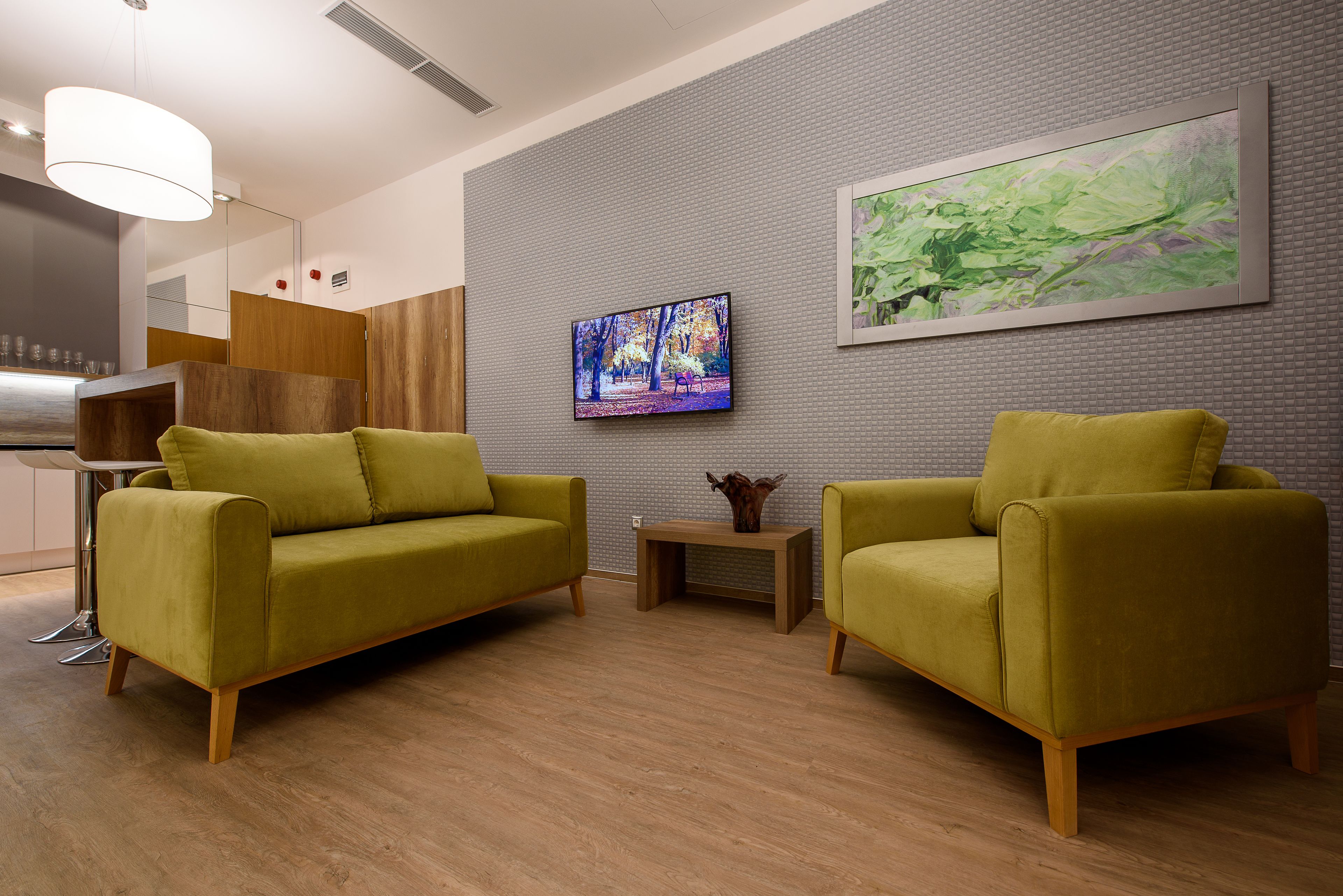 Una sala de estar moderna con dos sofás verdes, una mesa de centro de madera y un televisor de pantalla plana montado en la pared.