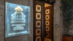 L’entrée d’un immeuble, avec une enseigne indiquant « Karoly Corner Residences », ainsi que les coordonnées et l’adresse du site web.