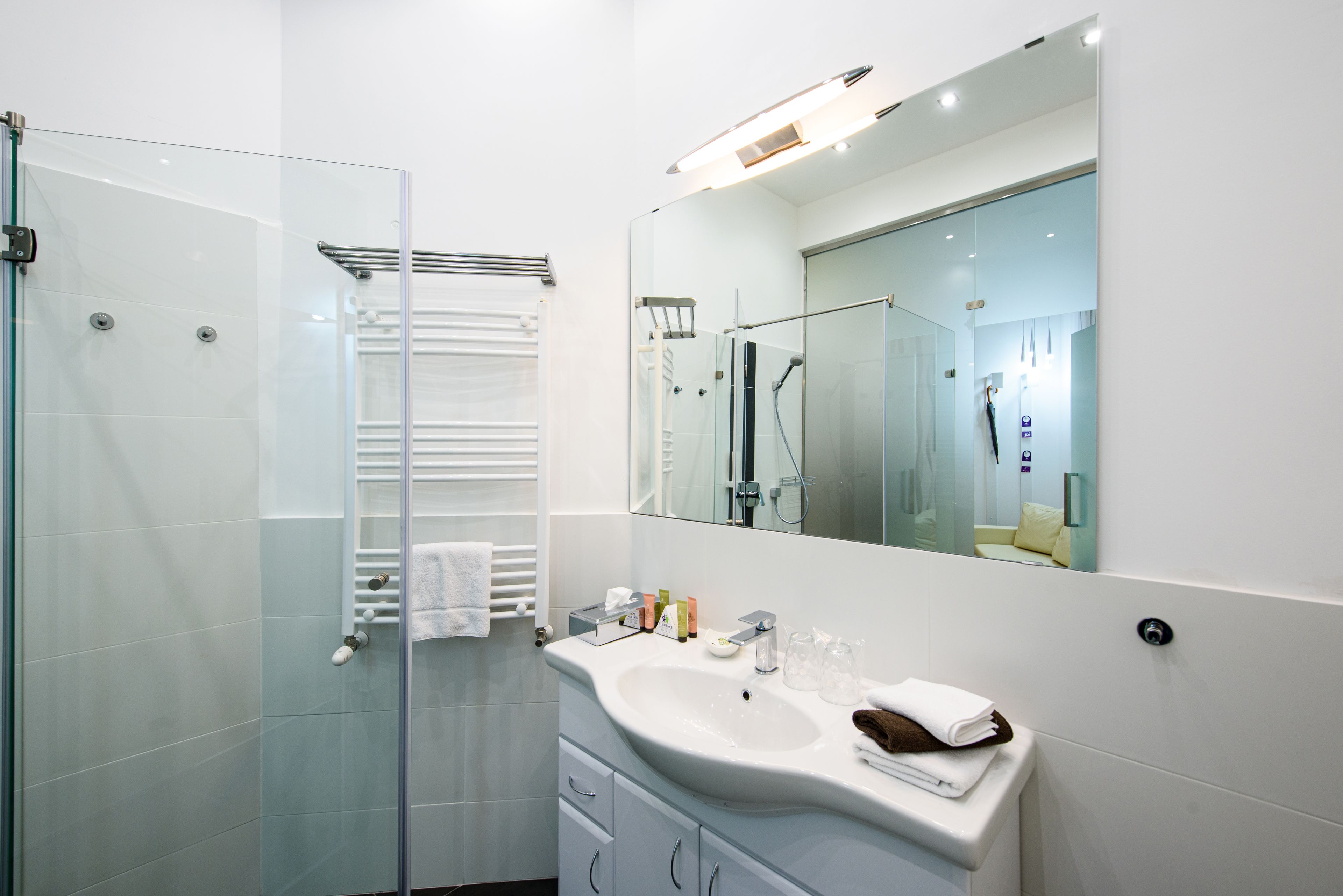 A modern bathroom with a glass shower enclosure, a white sink with toiletries, and a large mirror.