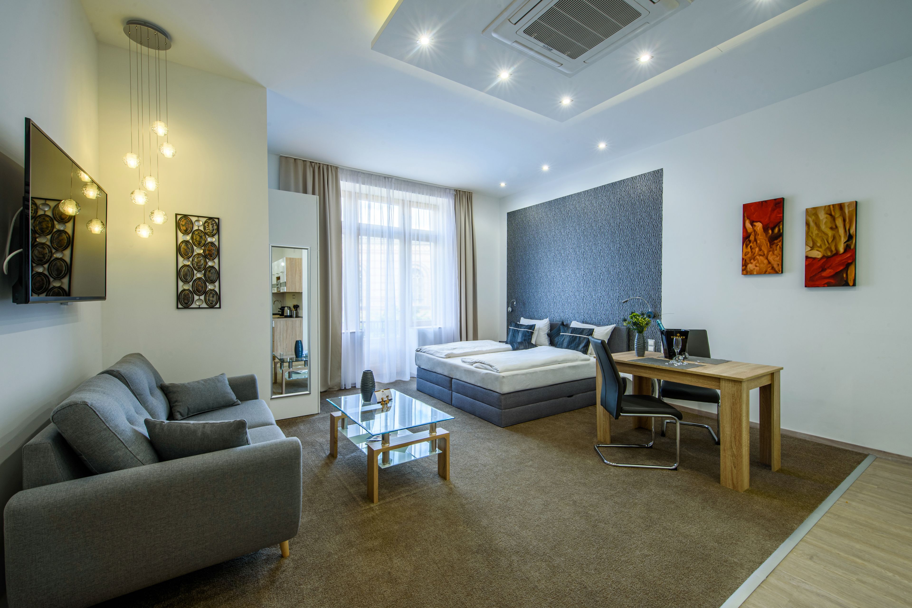 A modern, well-lit room with a sofa, a glass coffee table, a bed, a desk, and a chair.