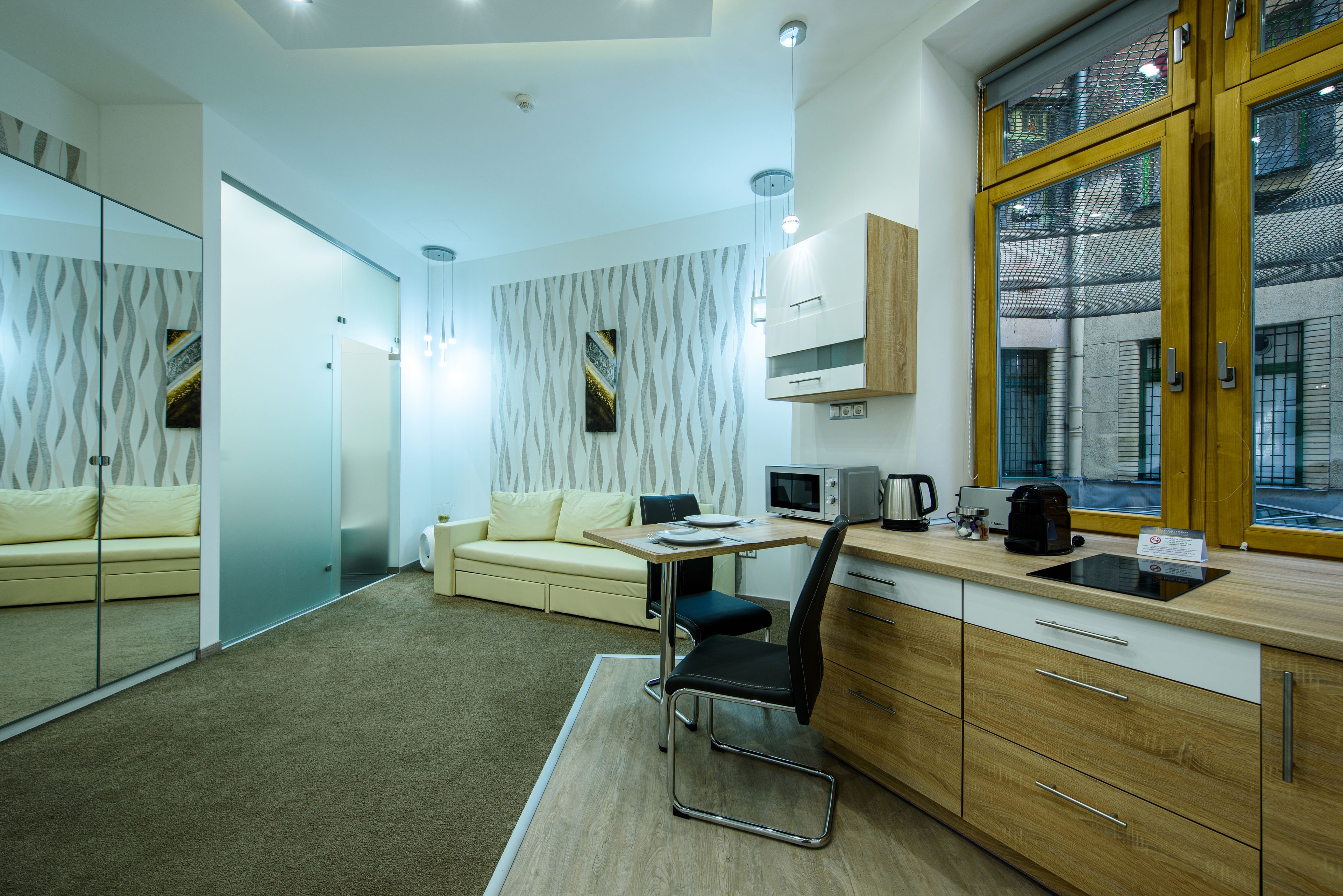 Una habitación compacta y moderna con kitchenette, un sofá, una mesa de comedor y un ventanal grande.