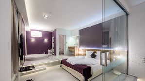 Une chambre moderne dotée d’une cloison en verre, d’un grand lit, d’une baignoire intégrée et d’une coiffeuse avec un miroir.