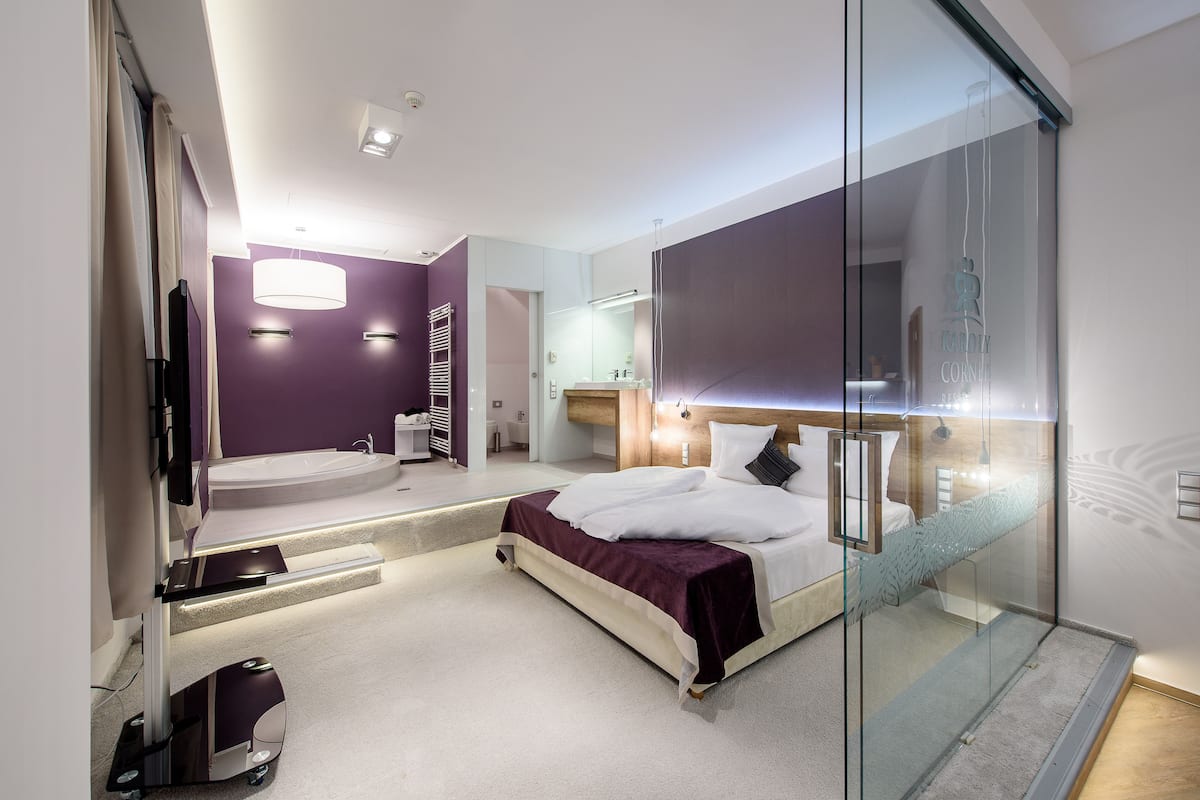 Ein modernes Schlafzimmer mit Glastrennwand, einem großen Bett, einer integrierten Badewanne und einem Schminktisch mit Spiegel.