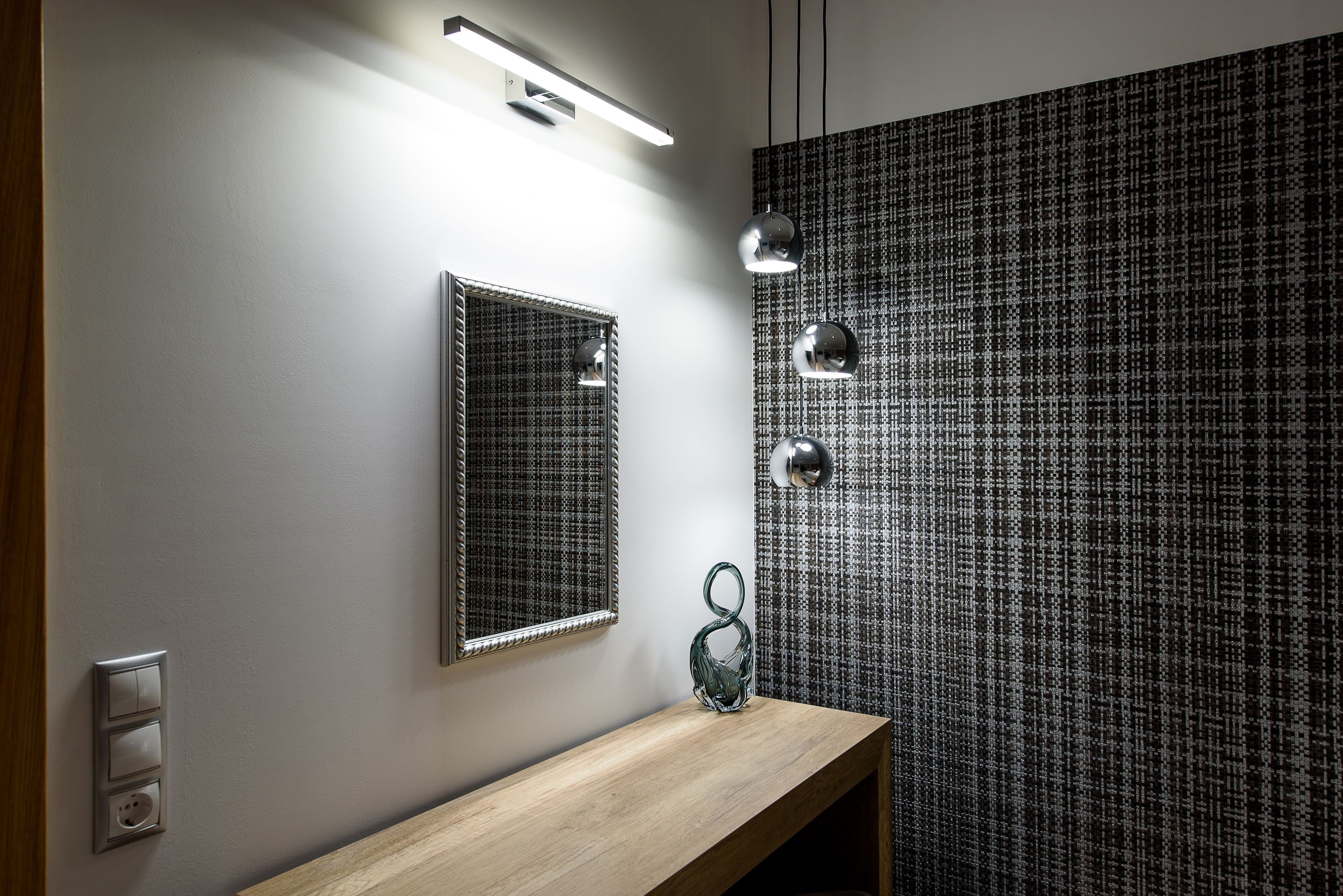 Ein Badezimmer mit einem Holzwaschtisch, einem Spiegel, einer Wandleuchte und einer Wand mit Muster.