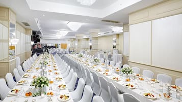 A banquet hall with long tables set for a formal event, featuring white tablecloths, chairs, and floral centerpieces.