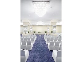 Un salón de conferencias con filas de sillas blancas, alfombra azul y una lámpara de araña grande.