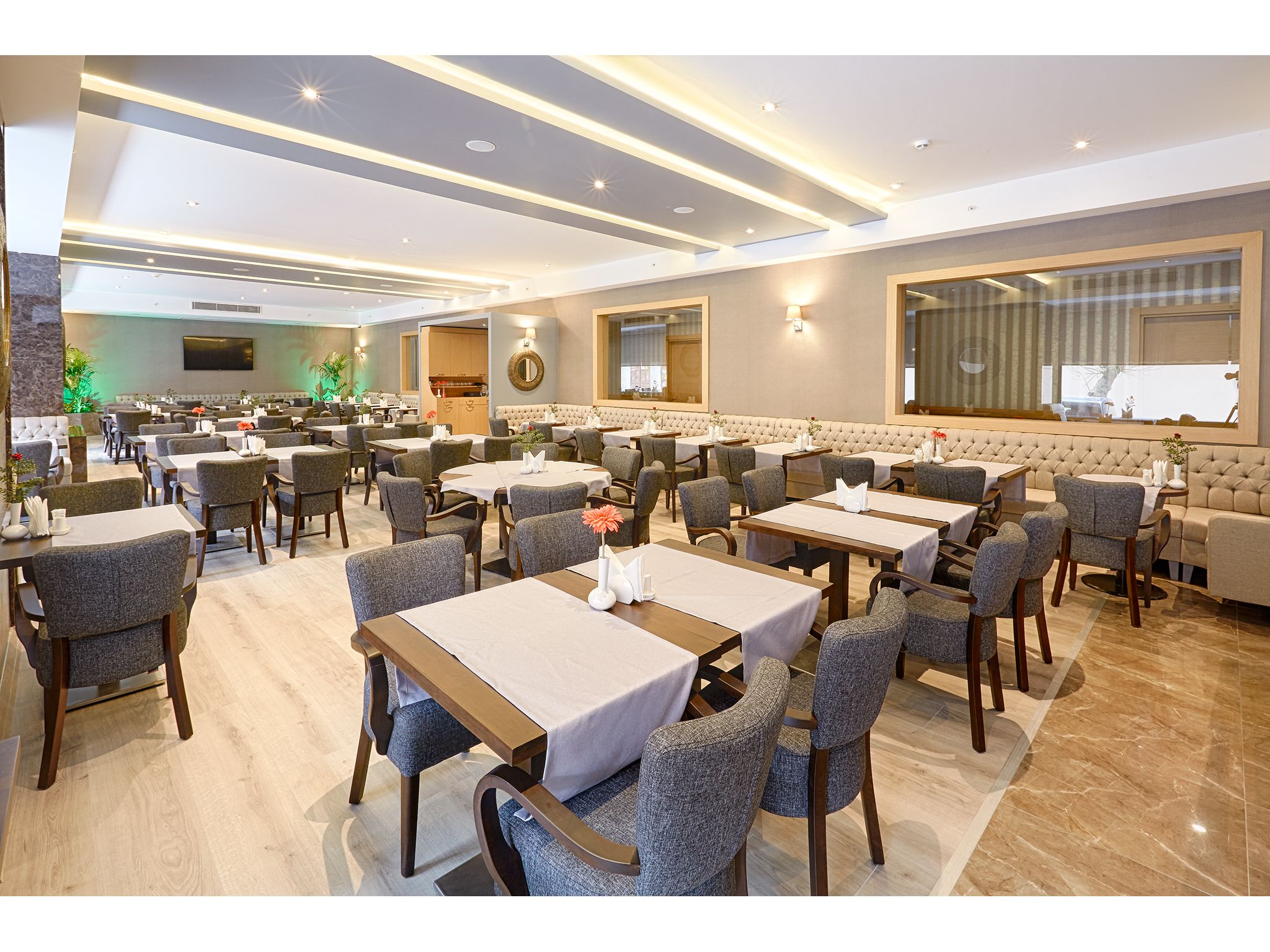 A spacious hotel dining area with multiple tables and chairs, a large mirror, and a television on the wall.