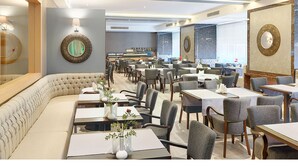 A spacious restaurant with multiple dining tables and chairs, a long cushioned bench, and decorative wall mirrors. - Kordon Hotel Cankaya (Izmir)