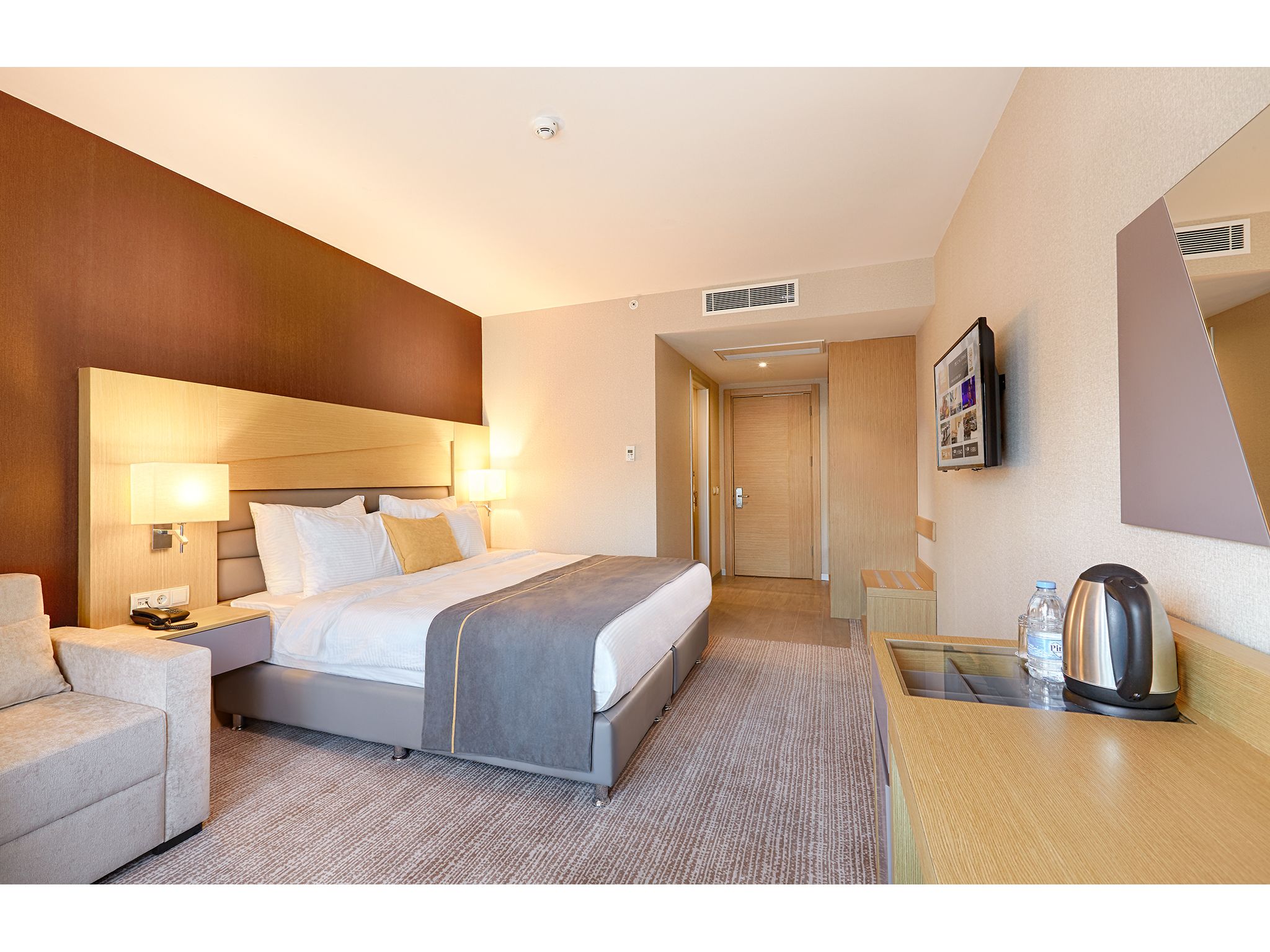A hotel room with a bed, bedside table, lamp, and a small seating area with a chair and table.