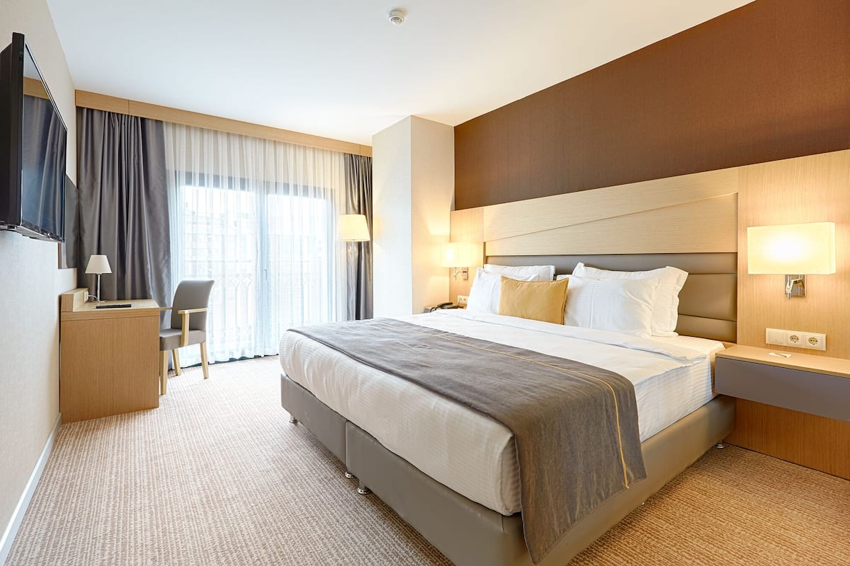 Ein Hotelzimmer mit einem großen Bett, Nachttischlampen, einem Schreibtisch mit Stuhl und Blick auf die Stadt durch das Fenster.