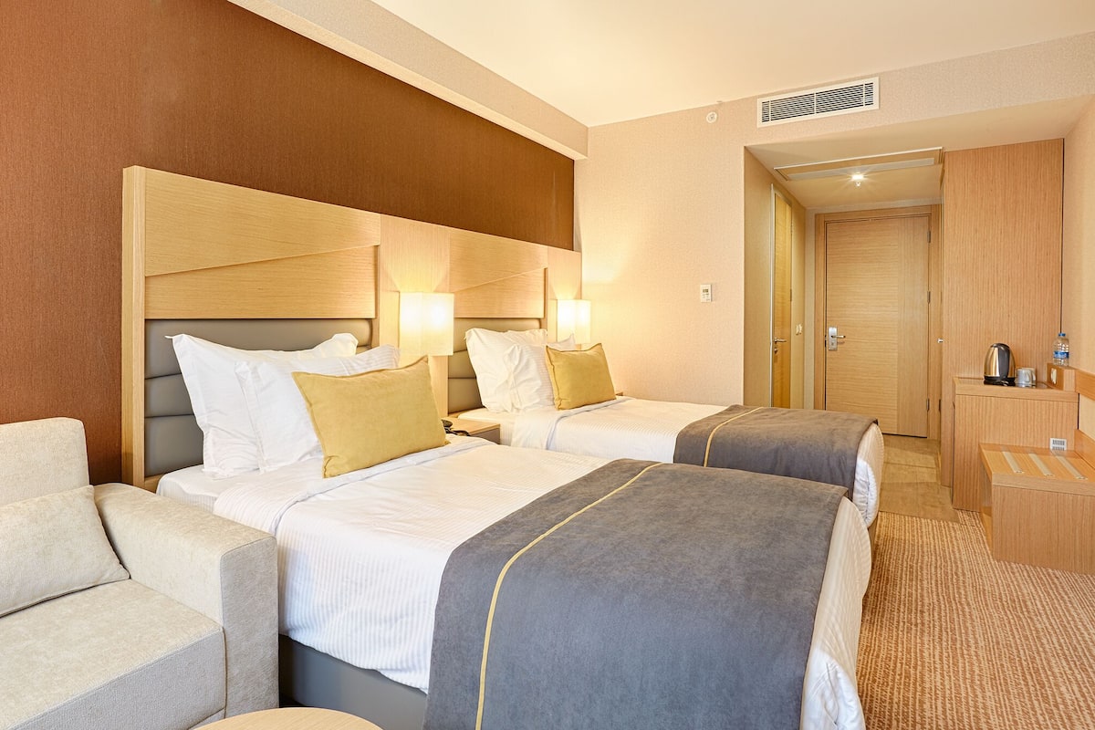 Ein Hotelzimmer mit zwei Betten, einer Sitzecke, einem Schreibtisch und einem Kleiderschrank.