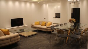 Uma sala de estar moderna com sofá, TV, mesa de centro de vidro e área de jantar com cadeiras e mesa.