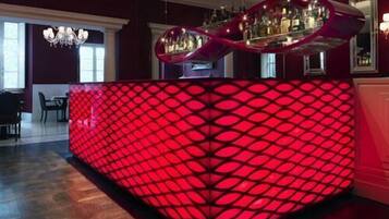 Un espace bar agrémenté d’une cloison rouge rétroéclairée et d’un comptoir où sont exposées des bouteilles.