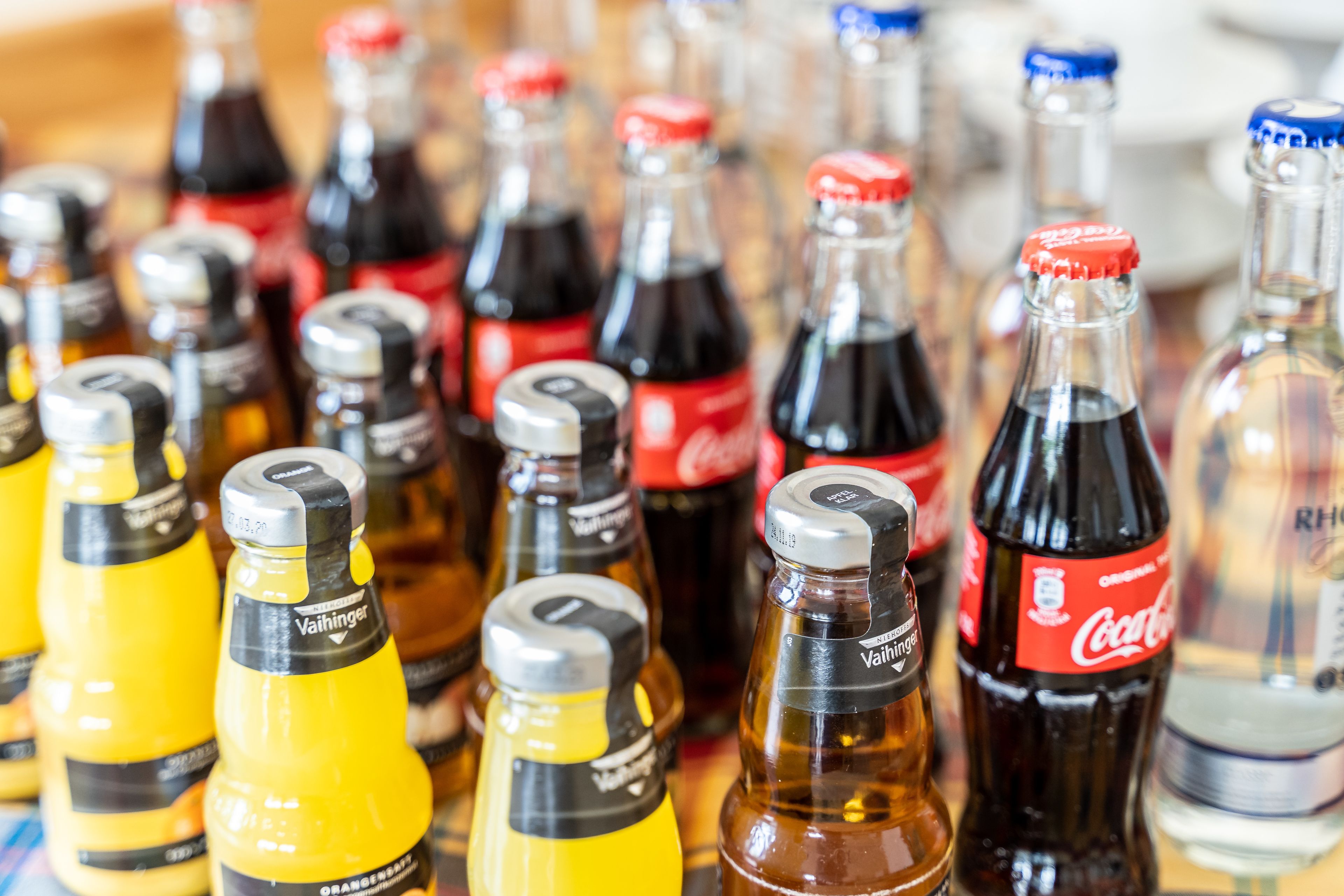 Un assortiment de bouteilles de boissons, notamment des bouteilles de Coca-Cola et de Vahhinger, disposées les unes à côté des autres.