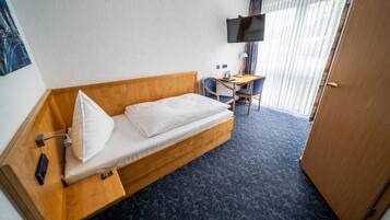 Een hotelkamer met een houten bed, een klein bureau, een stoel, een aan de muur bevestigde televisie en een raam met gordijnen.