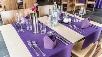 A dining table set with purple tablecloth, clear glassware, and silverware.