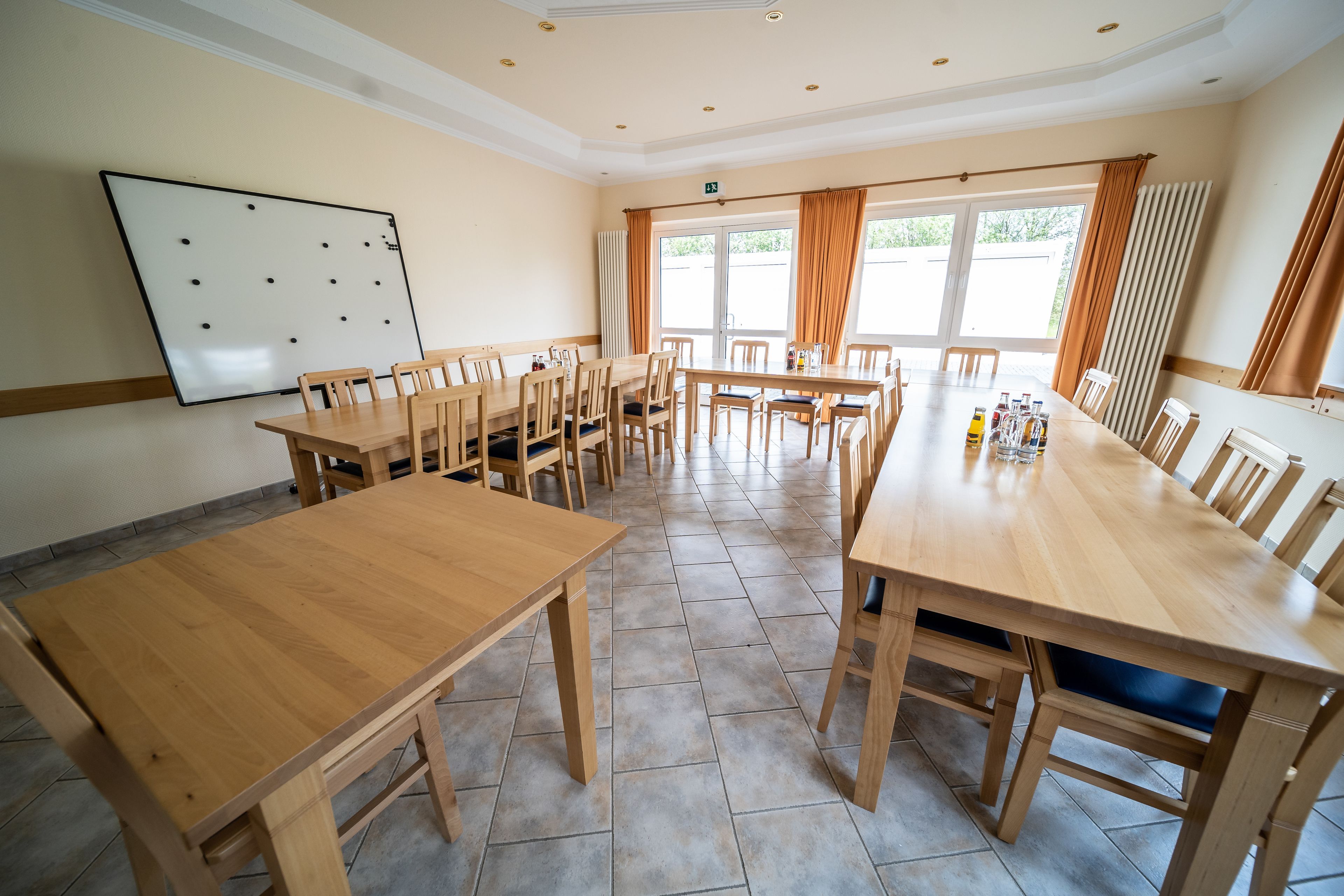 A conference room with multiple wooden tables and chairs, a whiteboard, and large windows with curtains.