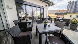 Un patio al aire libre con mobiliario de mimbre, una mesa con un florero y vistas a la ciudad.