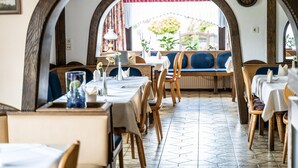 Un restaurante con mesas y bancos de madera, suelo de baldosas y vistas a través de un arco.