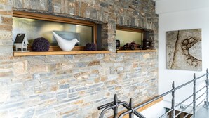 Un muro de piedra con dos ventanas, cada una con un repisa de madera que sostiene objetos decorativos. Se ve una barandilla de metal en primer plano.