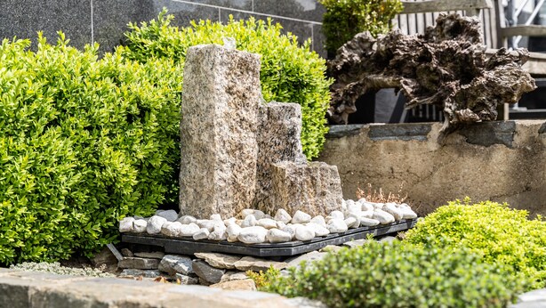 Un jardín ajardinado con una formación rocosa, arbustos cuidadosamente recortados y un sendero de piedra.
