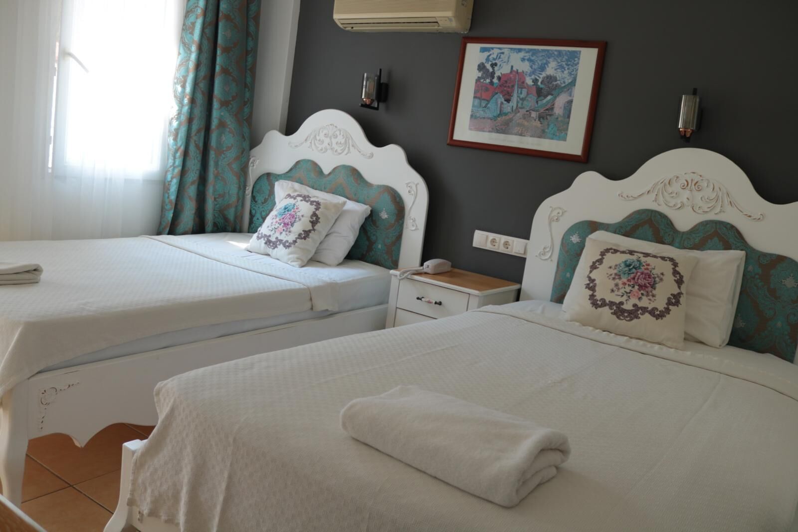 Une chambre d’hôtel avec deux lits, chacun doté d’une tête de lit blanche et d’oreillers assortis. On y trouve une table de chevet avec une lampe, ainsi qu’un tableau encadré accroché au mur.